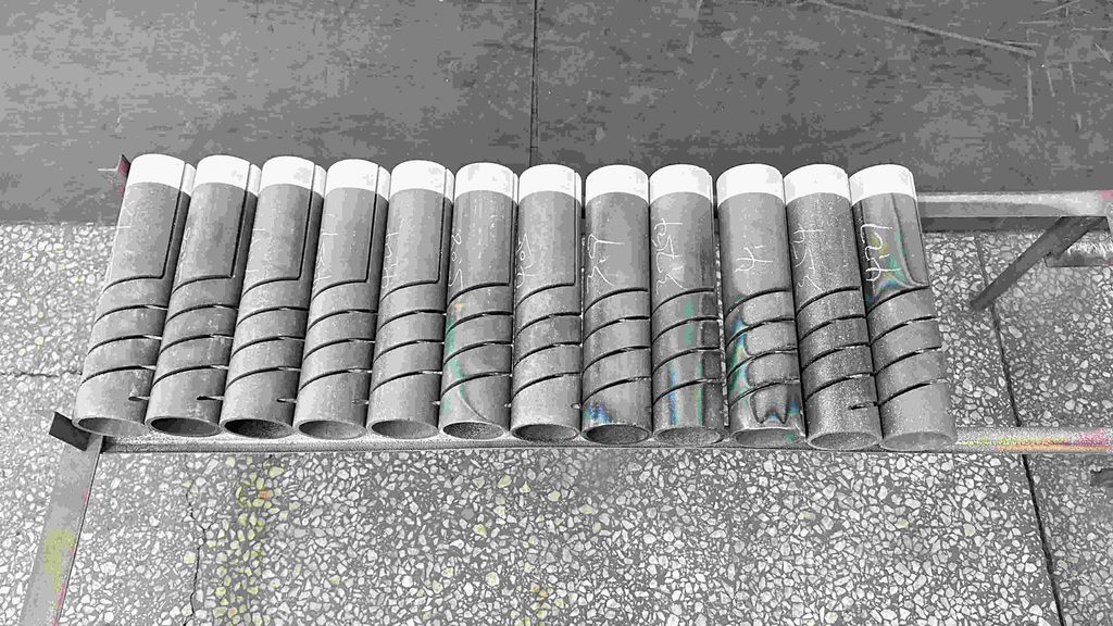 A row of cylindrical graphite components with machined slots arranged on a metal rack in a workshop