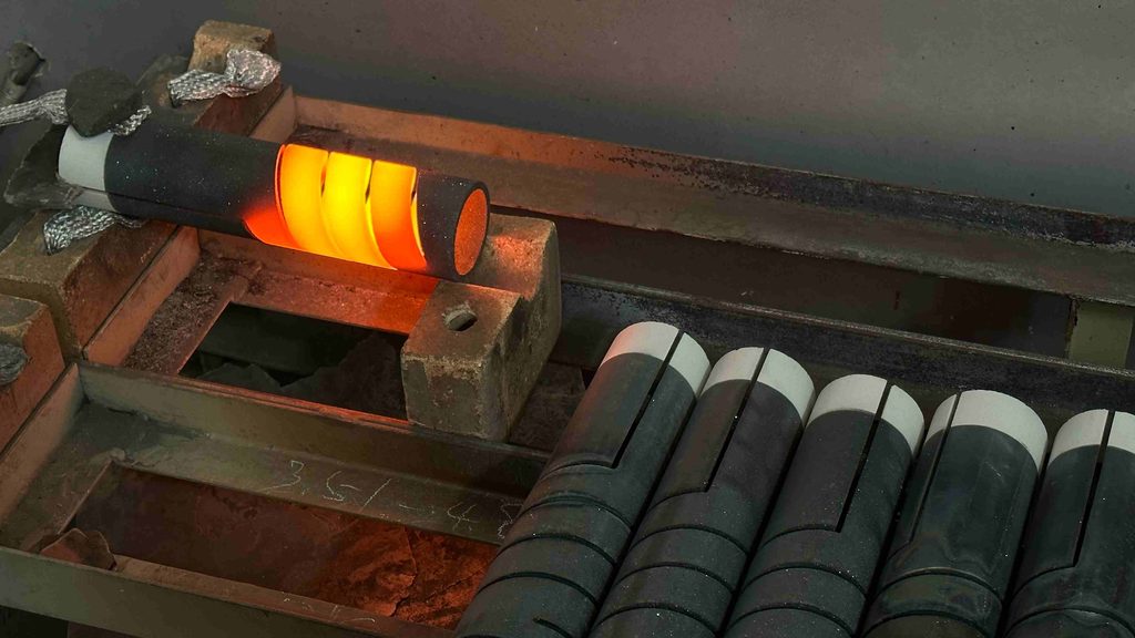 A heated cylindrical graphite component glowing orange during a high-temperature processing test, with similar components beside it
